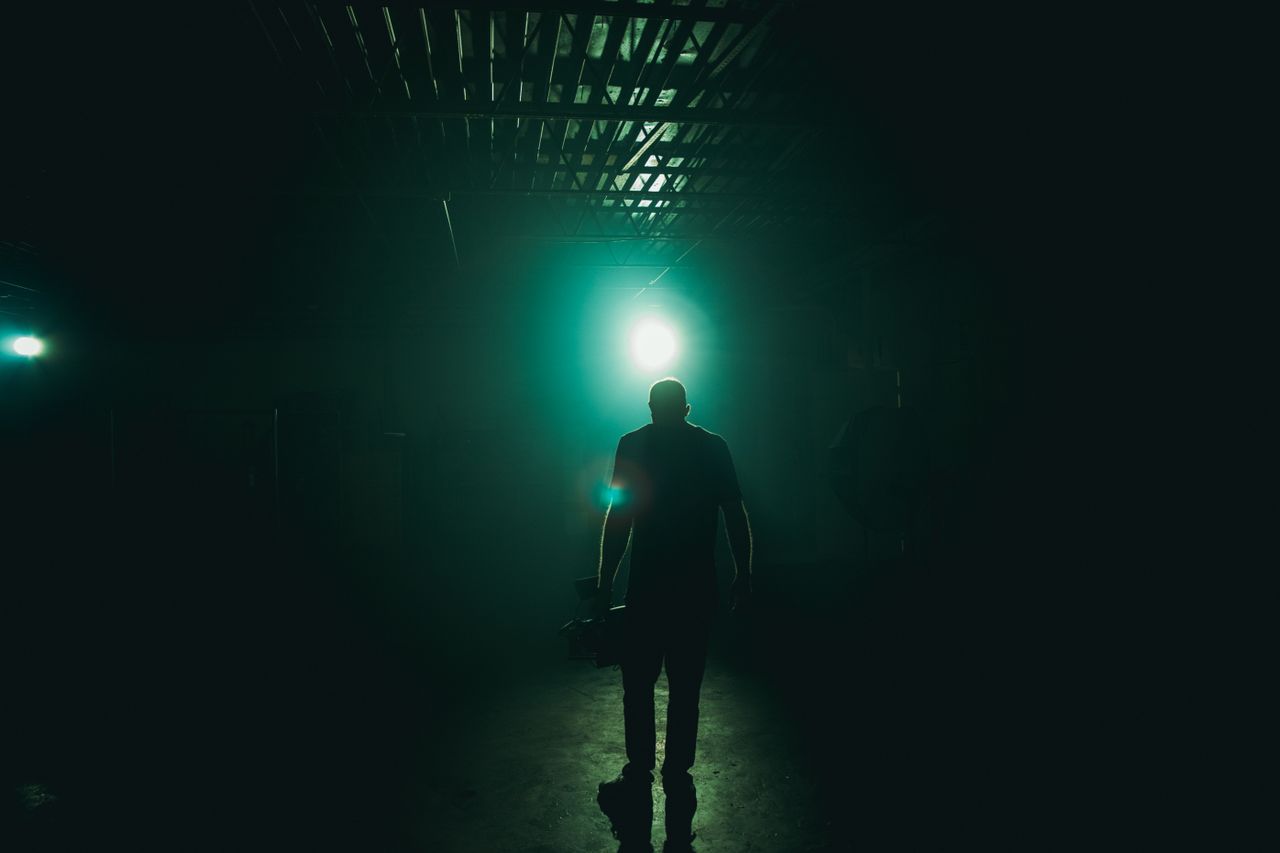 A silhouette of a cameraman holding equipment in a dark, illuminated room with a spotlight.