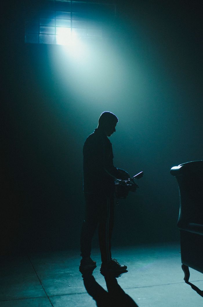 Silhouette of a man with camera in a dimly lit studio, dramatic light and shadow play.